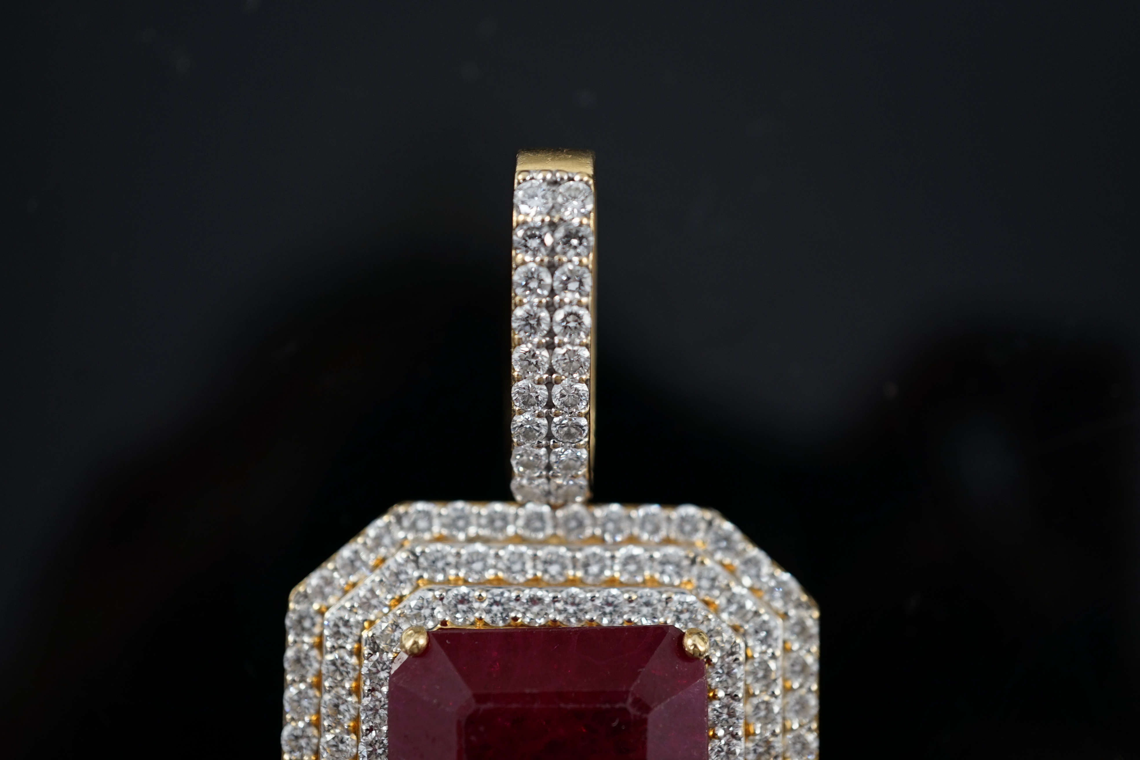 A large modern 18ct gold and single emerald cut synthetic ruby set pendant, bordered by three concentric bands of round brilliant cut diamonds